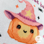 Kreuzstich Vorlagen Kürbis mit rosafarbenen Hexenhut umrandet von bunten Funkelsternen. Über dem Kürbis steht der Schriftzug Too cute to in rosa und schwarz mit zwei sich abseilenden Spinnen. Unter dem Kürbis steht in Großbuchstaben SPOOK in bunten Farben und schwarzen Schatten. Das Bild zeigt eine Nahaufnahme von dem Motiv.
