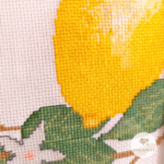 Kreuzstich Vorlagen Zitronenstrauch in frischen, sommerlichen gelb und grüntönen. Das Bild ist seitlich aufgenommen in Nahaufnahme um die Stickerei zu sehen. Ein Stück einer Zitrone, Blätter, Äste und die hellen Zitronenblüten.