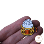 Cozy Pumpkin Mug Nadelmagnet als Stickzubehör zum Kreuzstich sticken. Ein Becher mit herbstlichen Kürbismotiv und Sahnehaube. Nadelmagnet liegt auf einer Hand um das Größenverhältnis darzustellen.