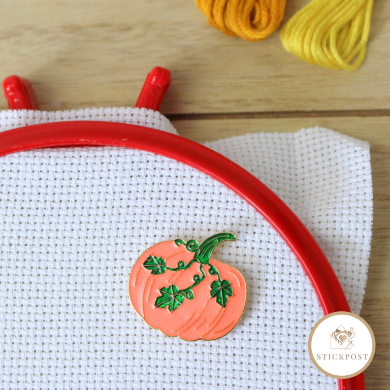 Herbstkürbis Nadelmagnet. orangefarbener Kürbis mit grünen Blätterranken. Magnethalterung auf Stoff im Stickrahmen gezeigt.