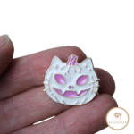 Pumpkin Kitty Nadelmagnet. Weiß und rosafarbene leicht schimmernde Kürbiskatze im Jack-o-lantern Stil. Nadelmagnet liegt auf einer Hand um das Größenverhältnis darzustellen.
