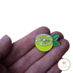 Lemon Love Nadelmagnet. Gelbe aufgeschnittene Zitrone mit grünen Blättern. Nadelmagnet liegt auf einer Hand um das Größenverhältnis darzustellen.