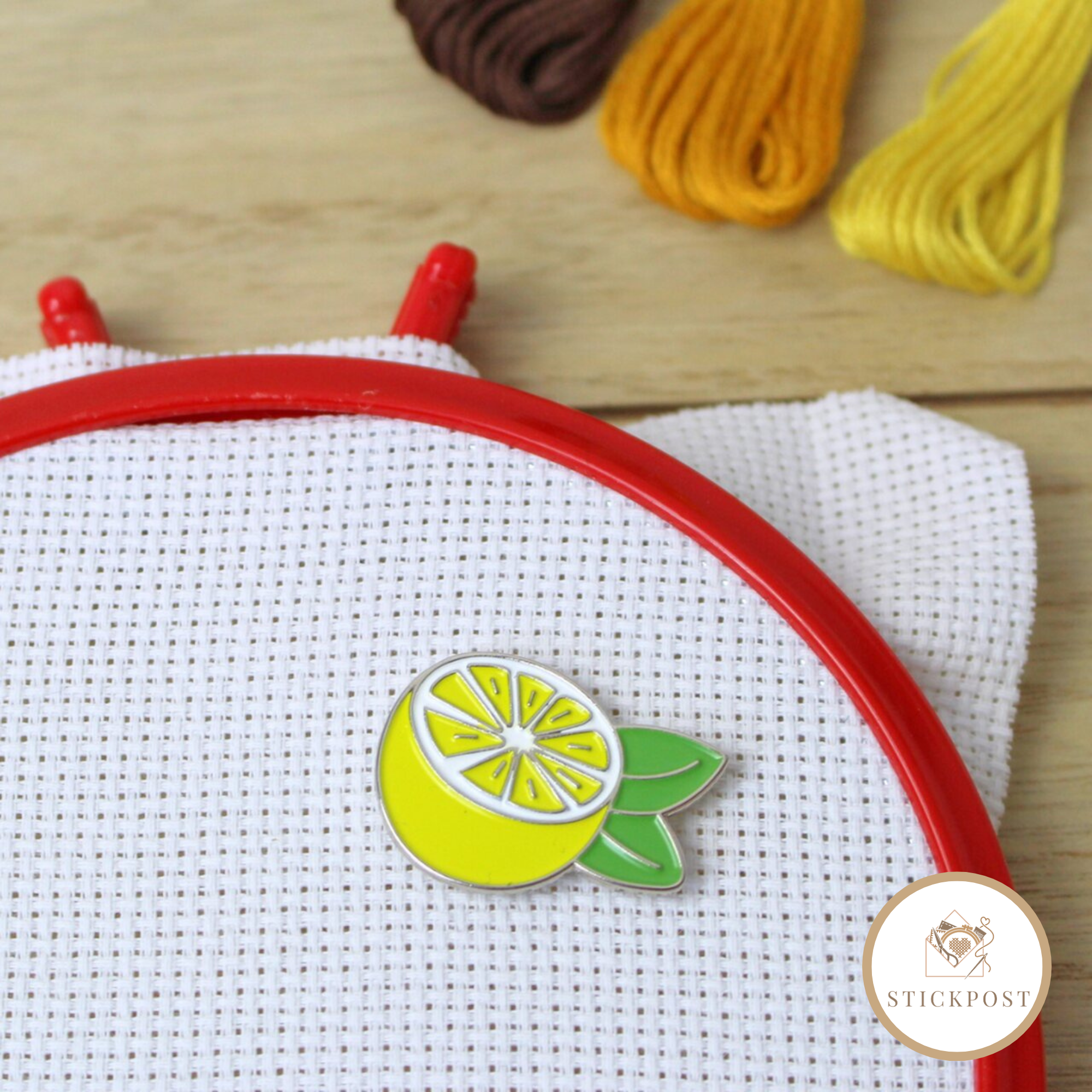 Stickpost Lemon Love Nadelmagnet Lemon Love Nadelmagnet. Gelbe aufgeschnittene Zitrone mit grünen Blättern. Magnethalterung auf Stoff im Stickrahmen gezeigt.