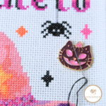 Pumpkin Kitty Nadelmagnet. Lila und rosafarbene Kürbiskatze im Jack-o-lantern Stil. Angewendet auf einem Stickbild. Zeigt wie die Magnethalterung die Sticknadel hält.